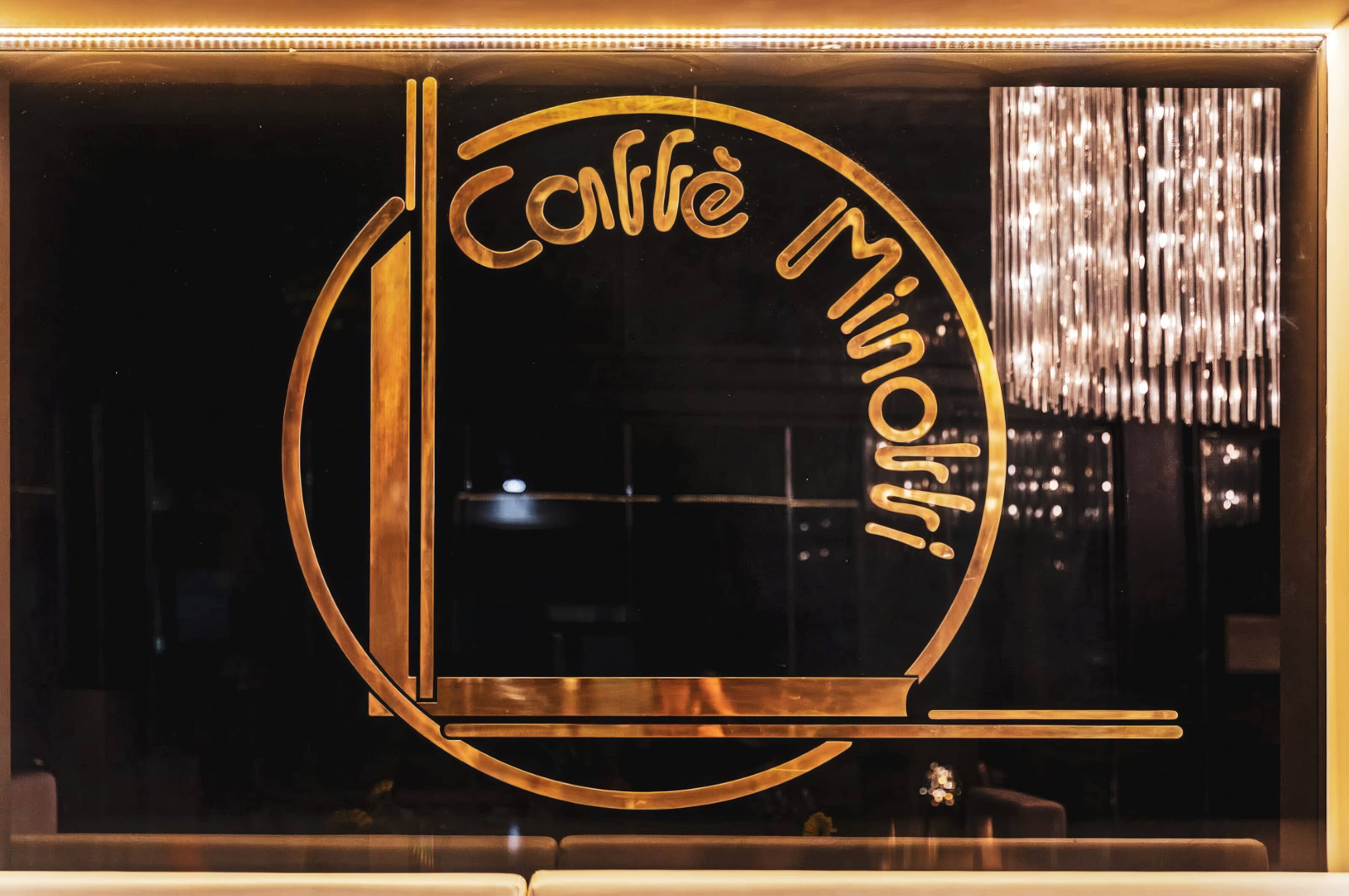 L'insegna in ottone del Caffè Minotti nel vetro, con il monogramma e la scritta